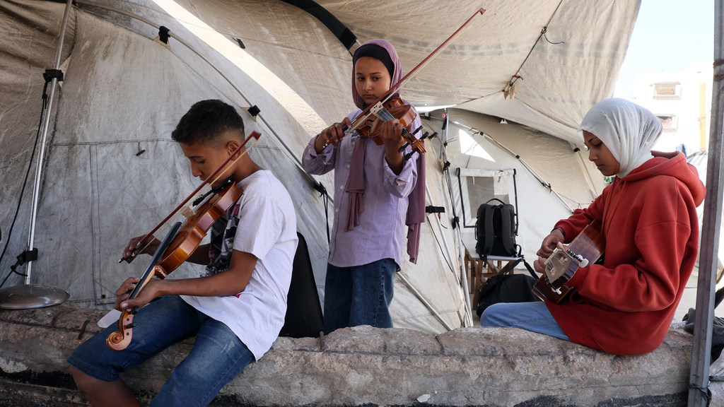Un niño y dos niñas tocan música dentro de una tienda de campaña en Gaza.